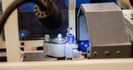 Nahaufnahme eines Werkzeugkopfs an einer technischen Maschine. Neben dem Werkzeug liegen Metallspäne auf der Arbeitsfläche. Ein schwarzer Lampenkopf beleuchtet den Arbeitsbereich