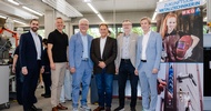Sechs Personen stehen in einer Werkstatt mit Maschinen und Arbeitsplätzen. Rechts befindet sich ein Roll-up mit der Aufschrift „Zukunftsjob Metalltechniker:in“. Das Roll-up zeigt eine Person mit Schweißhelm sowie ein Detailbild eines Türschlosses mit Schlüssel