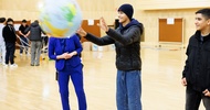 Drei Personen stehen nebeneinander. Eine Person ist dabei einen Ball zu fangen, auf dem die Erde abgebildet ist