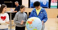 Ein Teenager hält einen Globus. Daneben stehen zwei weitere Teenager. Alle blicken darauf