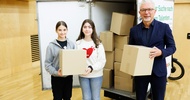 Porträt von zwei Kindern und einer erwachsenen Person. Alle drei halten einen kleinen Karton