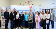 Porträt von vierzehn Personen, die vor einem Plakat stehen, auf dem unter anderem Berufsschule für Schönheitsberufe und Tauch ein in deine berufliche Zukunft steht