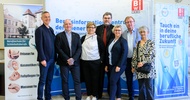 Porträt von sieben Personen, die vor einem Plakat stehen, auf dem unter anderem Berufsschule für Schönheitsberufe und Tauch ein in deine berufliche Zukunft steht