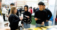Fünf Jugendliche stehen auf einer Messe neben einem Tisch, auf dem verschiedene Werkzeuge zur Metallbearbeitung sind. Im Hintergrund sind weitere Personen, die hinter und neben Tischen stehen