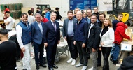 Porträt von mehreren Personen, die nebeneinander auf einer Messe stehen. Hinter den Personen sind weitere Personen und Jugendliche sowie verschiedene Bauutensilien wie eine Scheibtruhe