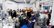 Aufnahme einer Metallwerkstatt aus der Vogelperspektive. Im Raum stehen an verschiedenen Geräten kleinere Gruppen mit Erwachsenen sowie jugendlichen Personen