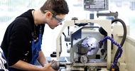 Eine Person mit Schutzbrille und blauer Latzhose bedient ein Gerät in einer Werkstatt
