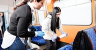 Zwei Personen mit Handschuhen stehen in einer leeren U-Bahn neben gepolsteter Sitze und reinigen diese