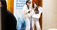 Zwei Teenager mit dunklen Haaren, hellen Westen und Hosen posieren für ein Foto. Die linke Person trägt eine Sonnenbrille. Die rechte Person hat ienen Haarreifen mit Herzen in den Haaren