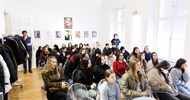 In einem Publikum mit mehreren Reihen sitzen viele Teenager sowie ein paar Erwachsene. An der Wand hängen Coverseiten verschiedener Magazine in Bilderrahmen