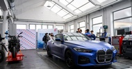 In einer Werkstatt steht ein blaues Auto. Daneben stehen mehrere Jugendliche
