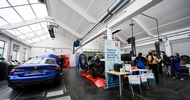 In einer Werkstatt steht ein blaues Auto. Daneben stehen mehrere Jugendliche