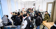 In einem Raum mit verschiedenen Maschinen stehen viele Kinder bzw. Jugendliche mit Rucksacken
