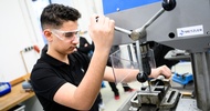  Eine Person mit Schutzbrille steht neben einer Bohrmaschine und betätigt diese