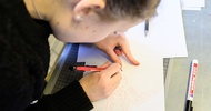 Eine Person malt mit einem Stift etwas auf einem Blatt Papier