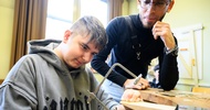  Eine jugendliche Person steht an einem Tisch und sägt mit einer Handsäge an einem Stück Holz herum