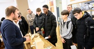 Auf einem Tisch sind verschiedene Werkstücke aus Holz wie eine Lade. Neben dem Tisch stehen mehrere Jugendliche
