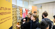 Zwei jugendliche stehen vor einer Plakat, auf der verschiedene Felle und Häute von Tieren hängen wie von einem Schaf oder von einer Echse