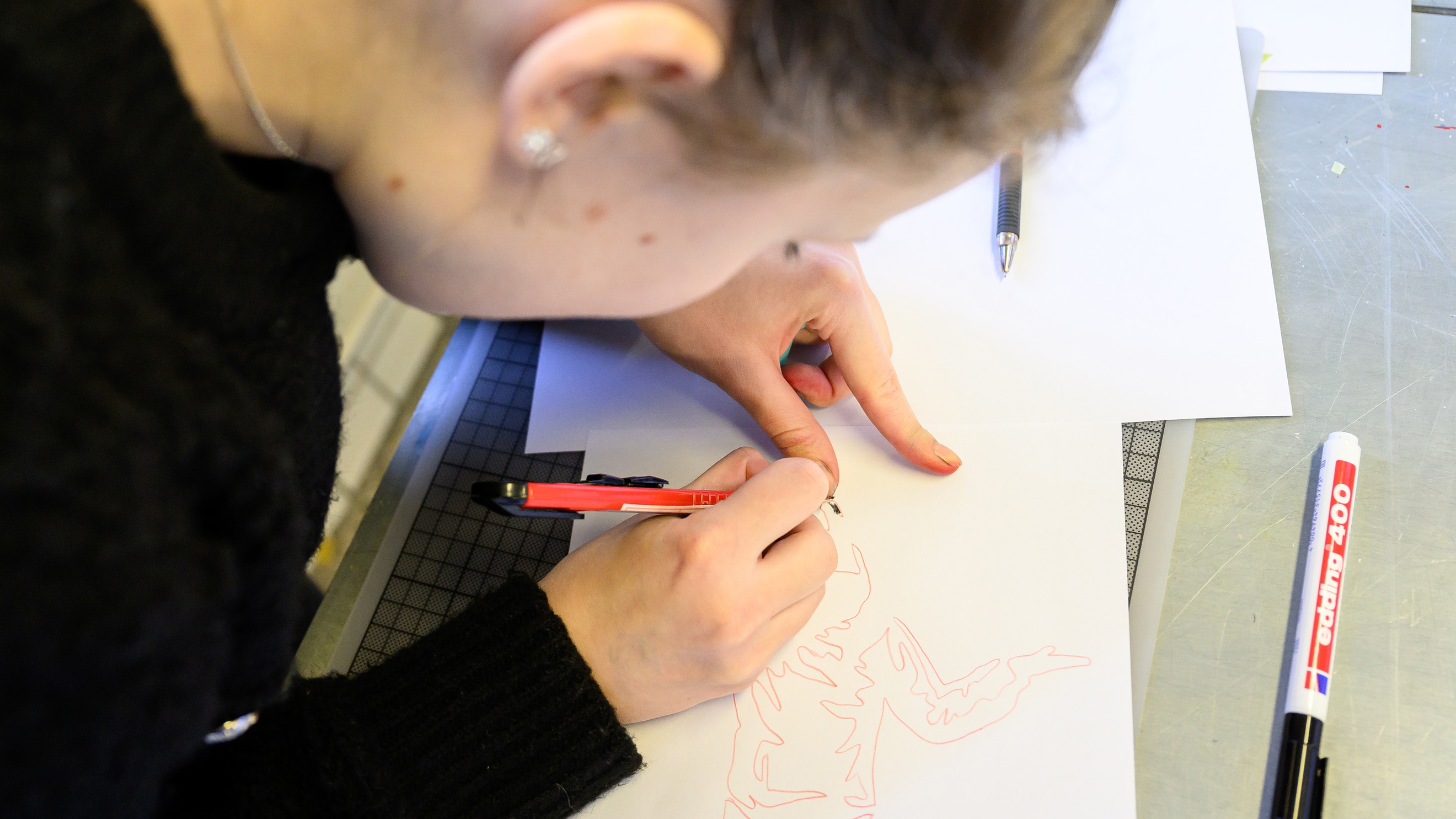 Eine Person malt mit einem Stift etwas auf einem Blatt Papier