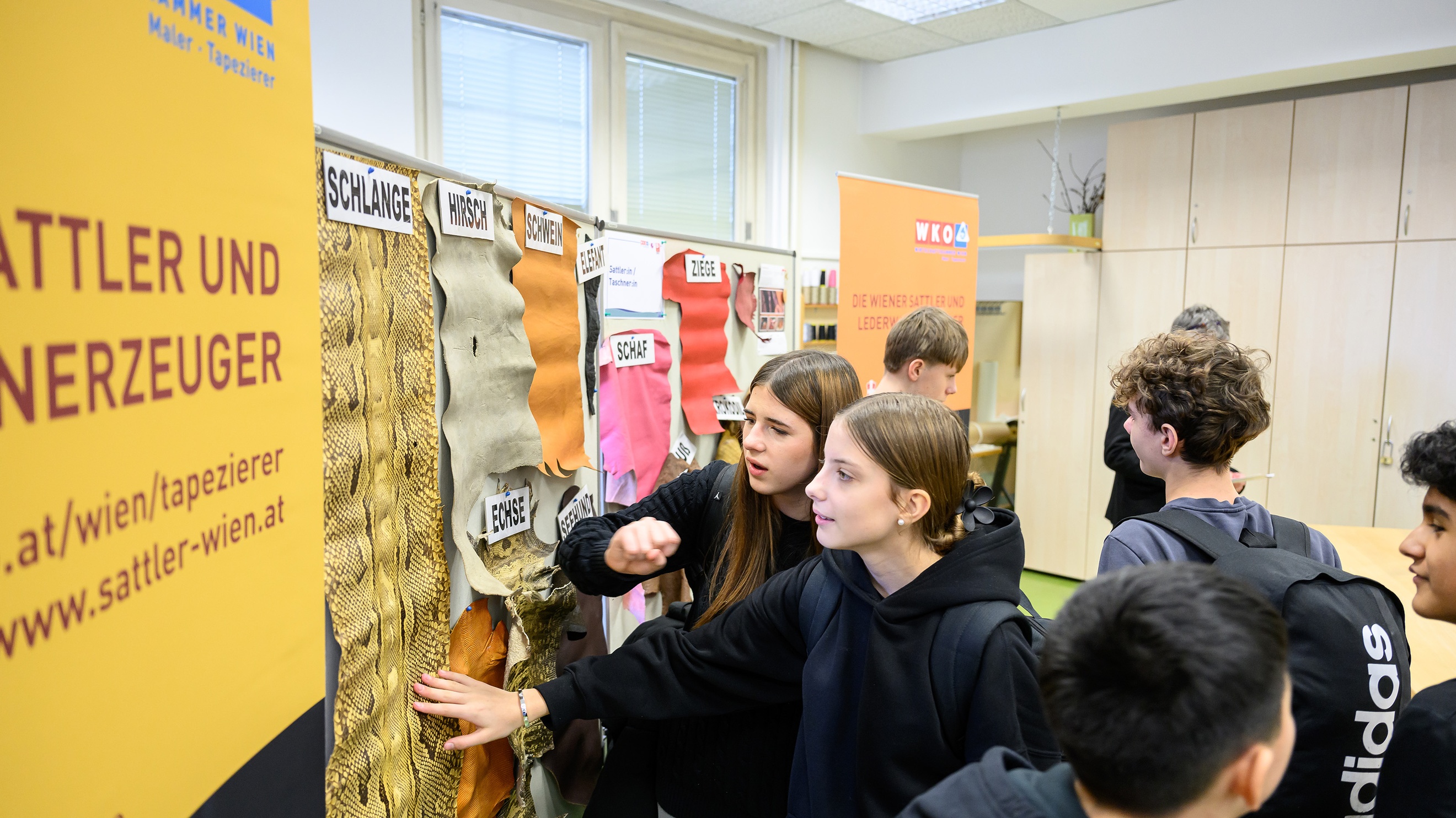 Zwei jugendliche stehen vor einer Plakat, auf der verschiedene Felle und Häute von Tieren hängen wie von einem Schaf oder von einer Echse