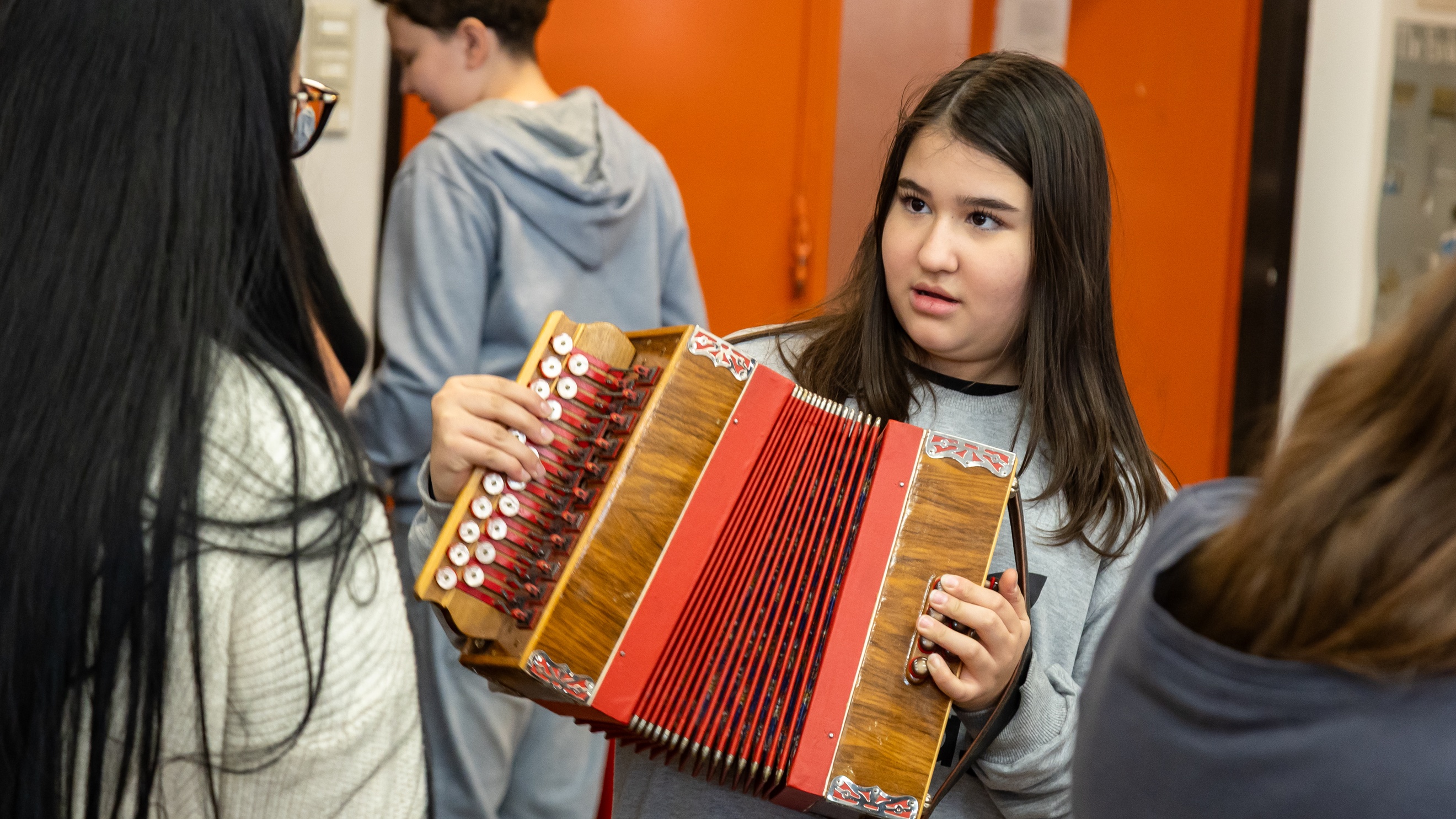 Eine jugendliche Person hält ein Akkordeon und blickt zu einer anderen Person, die ihr gegenüber steht
