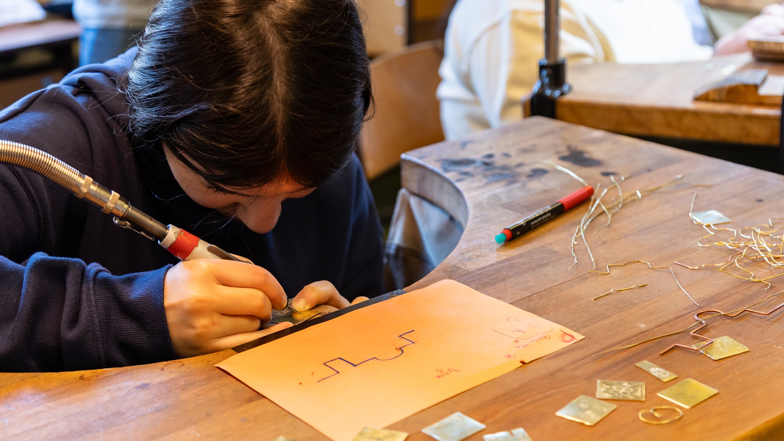 Eine jugendliche Person befestigt mit einem Klebestift dünne Metallfäden auf einem dünnen Stück Metall