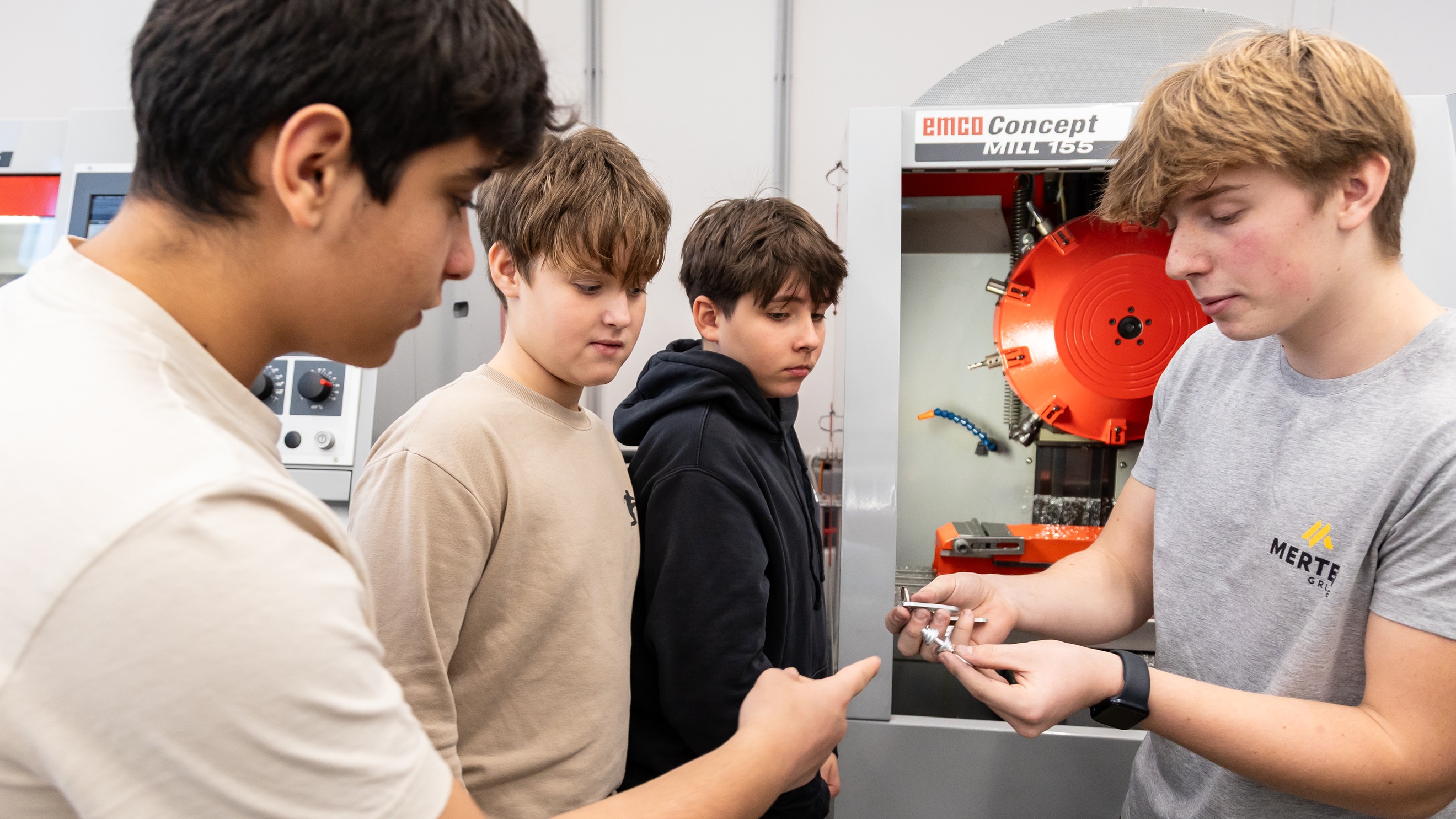 Drei jugendliche Personen stehen einer jugendlichen Personen gegenüber, die kleine Metallteile hält