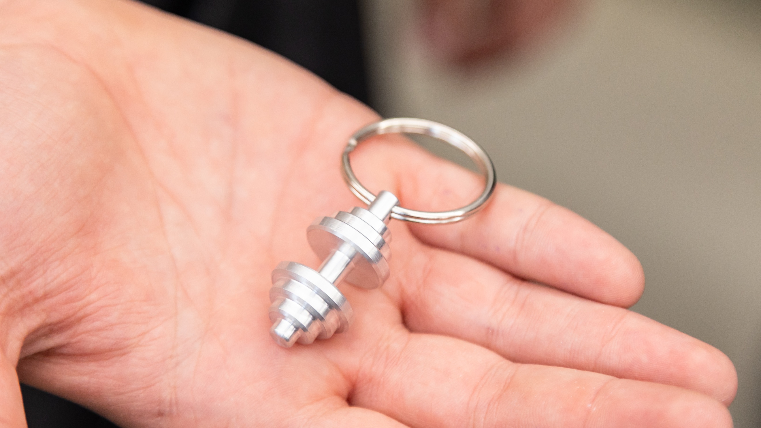 Nahaufnahme der Hand einer Person, auf der ein Schlüsselanhänger mit einer kleinen Hantel liegt