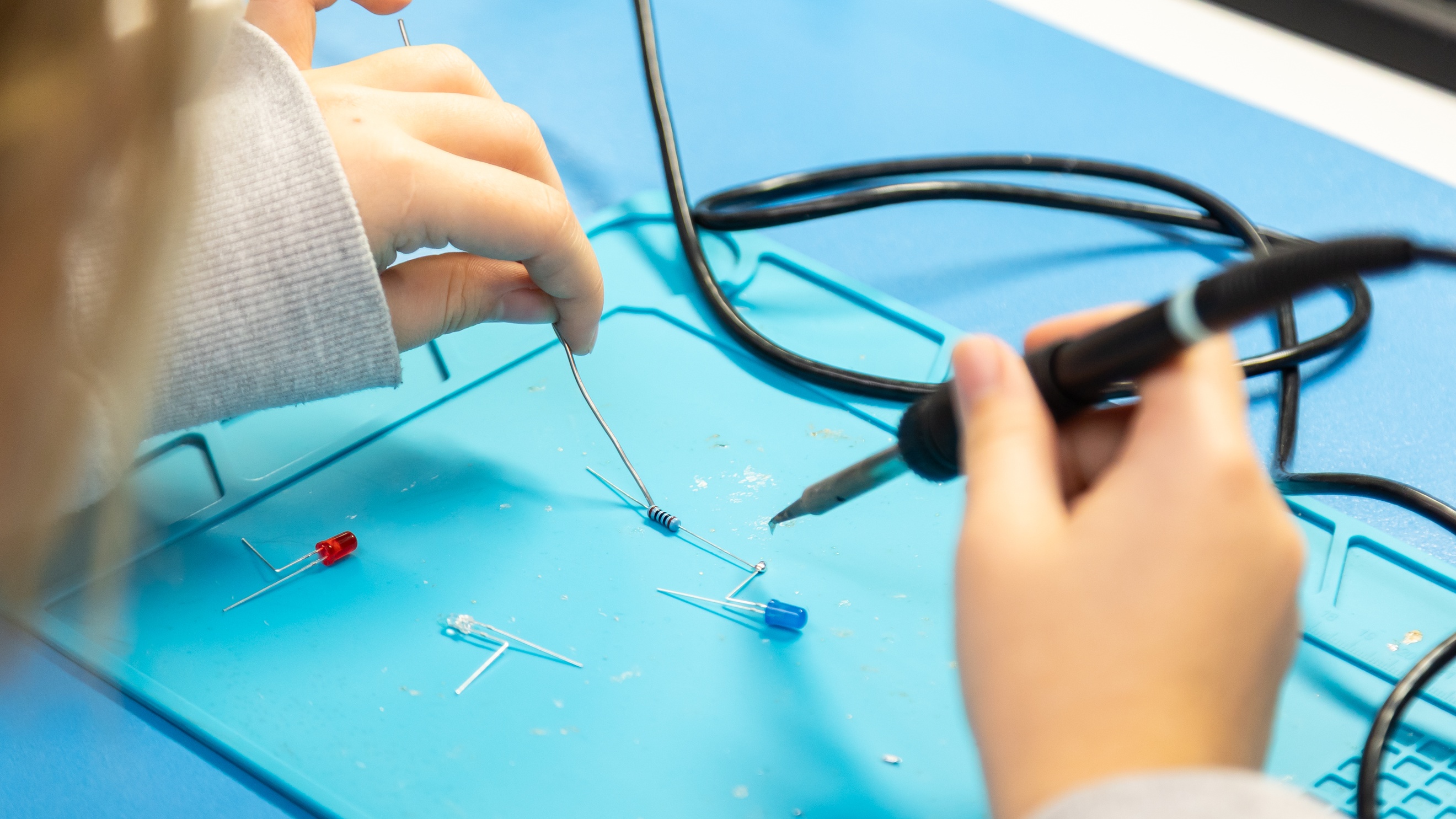 Nahaufnahme der Hände eines Kindes, das mit einer feinen Klebepistole Elektroden mit Drähten verbindet