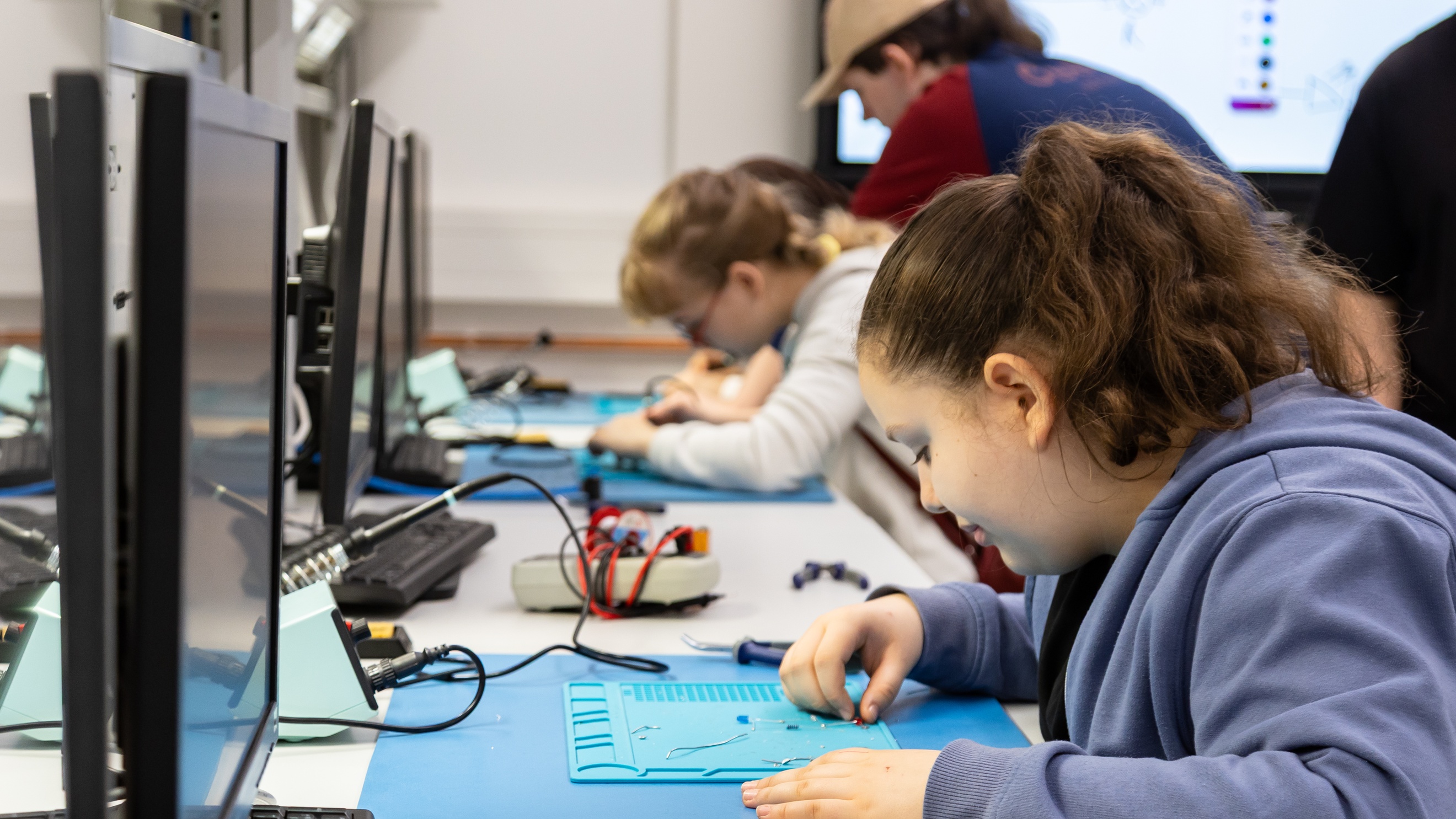 Ein Kind sitzt an einem Tisch. Auf dem Tisch liegen verschiedene Elektroden und Werkzeug