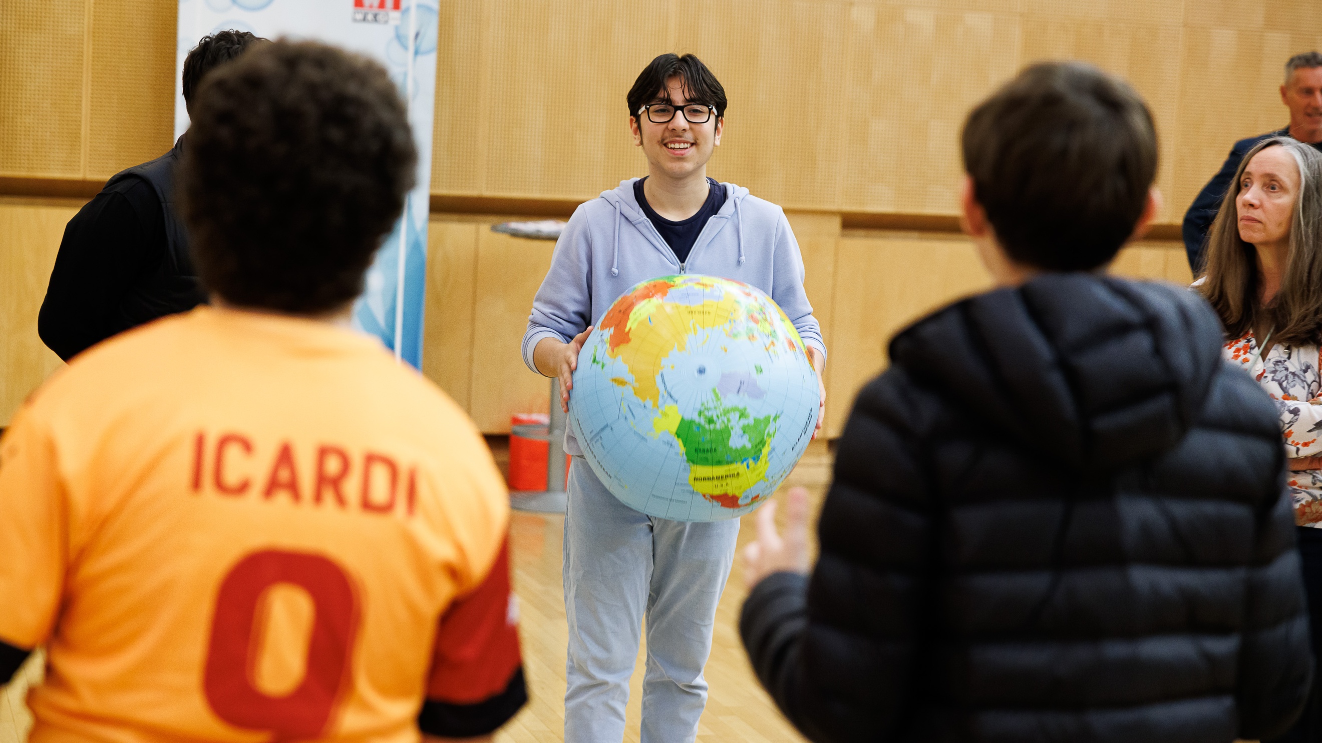 Mehrere Personen stehen in einem Kreis. Eine Person hält einen Ball, auf dem die Erde abgebildet ist