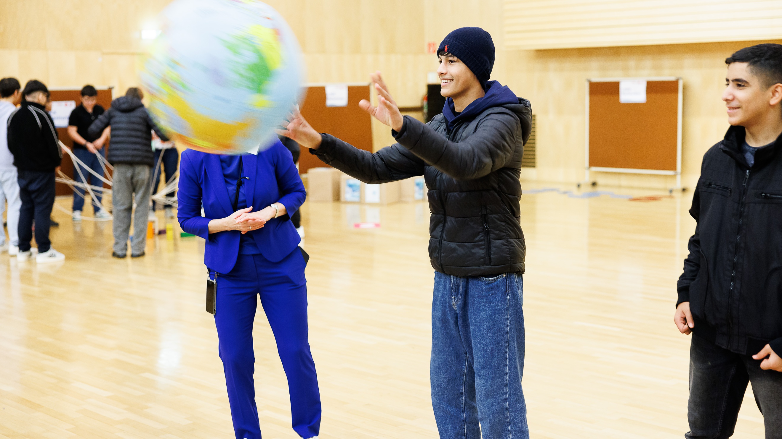 Drei Personen stehen nebeneinander. Eine Person ist dabei einen Ball zu fangen, auf dem die Erde abgebildet ist