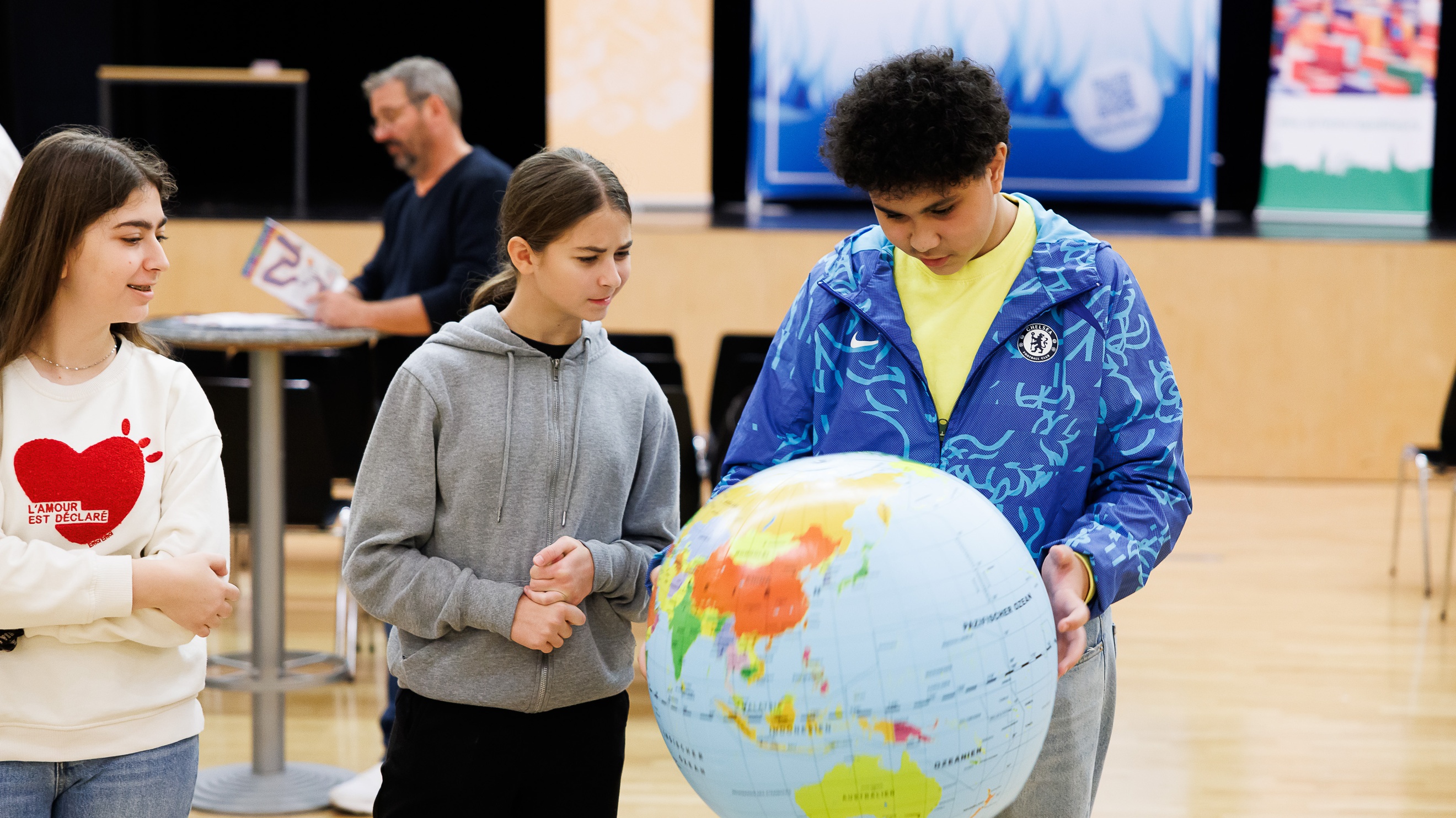 Ein Teenager hält einen Globus. Daneben stehen zwei weitere Teenager. Alle blicken darauf