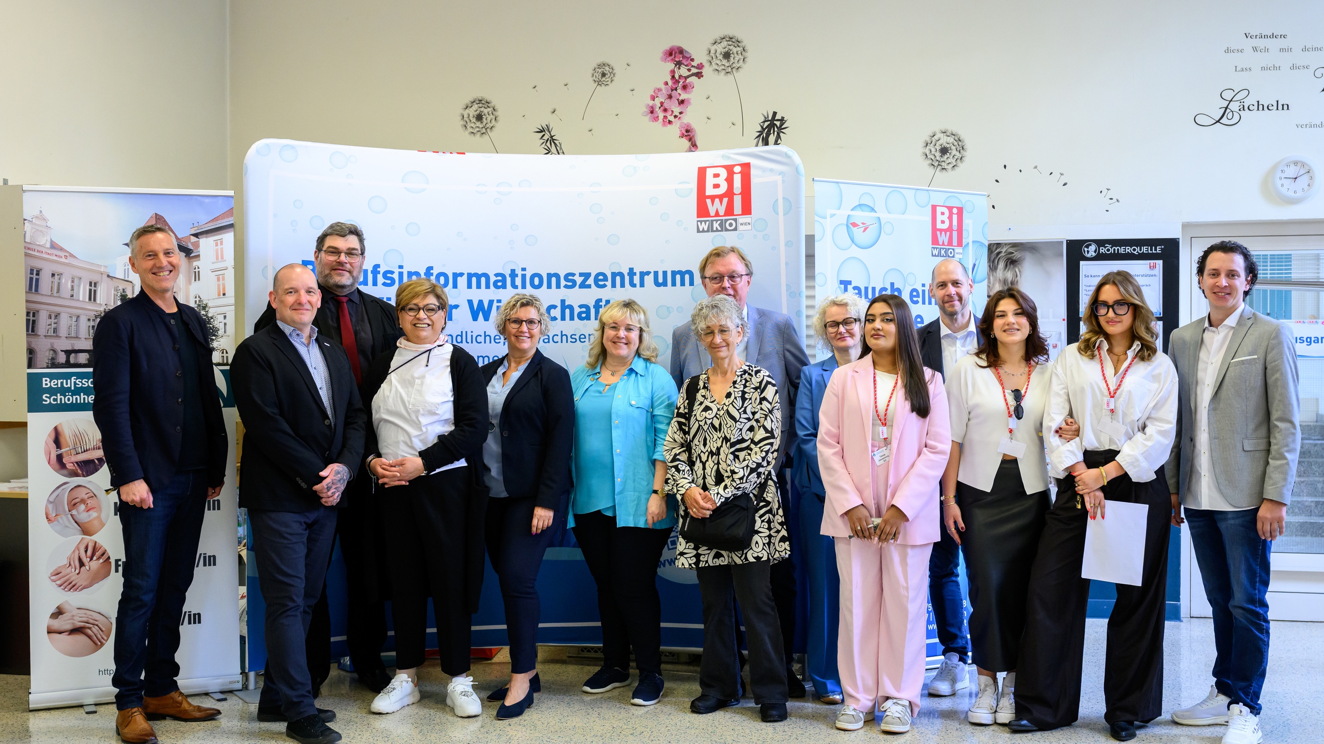 Porträt von vierzehn Personen, die vor einem Plakat stehen, auf dem unter anderem Berufsschule für Schönheitsberufe und Tauch ein in deine berufliche Zukunft steht