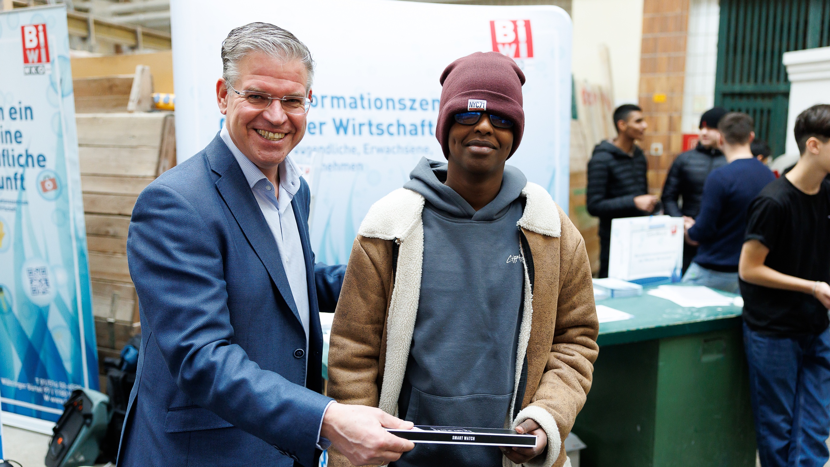 Porträt einer erwachsenen und einer jugendlichen Person. Hinter den beiden Personen ist ein Banner 