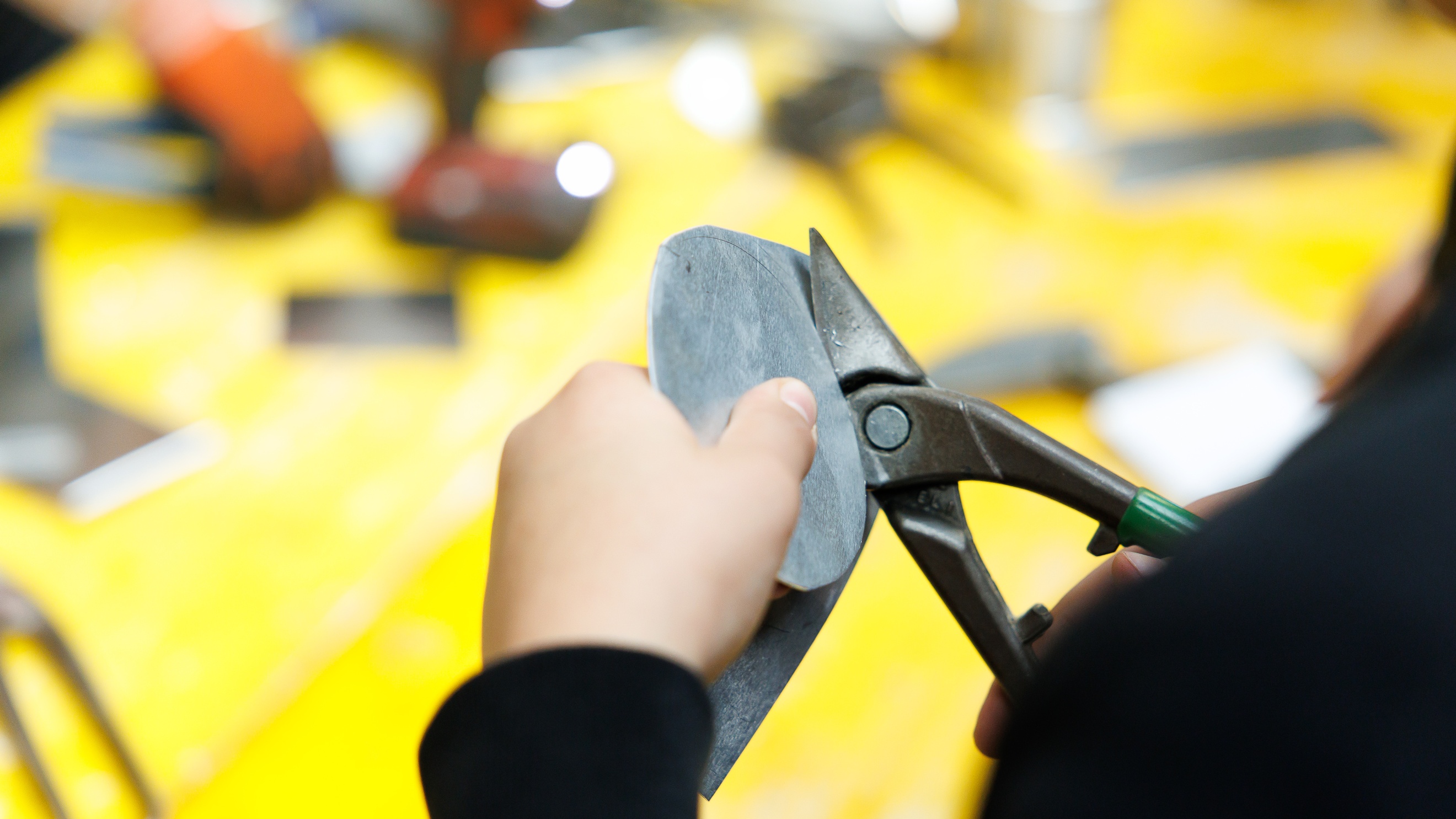 Nahaufnahme der Hände einer Person, die ein flaches Metallstück mit einer Metallschere schneidet