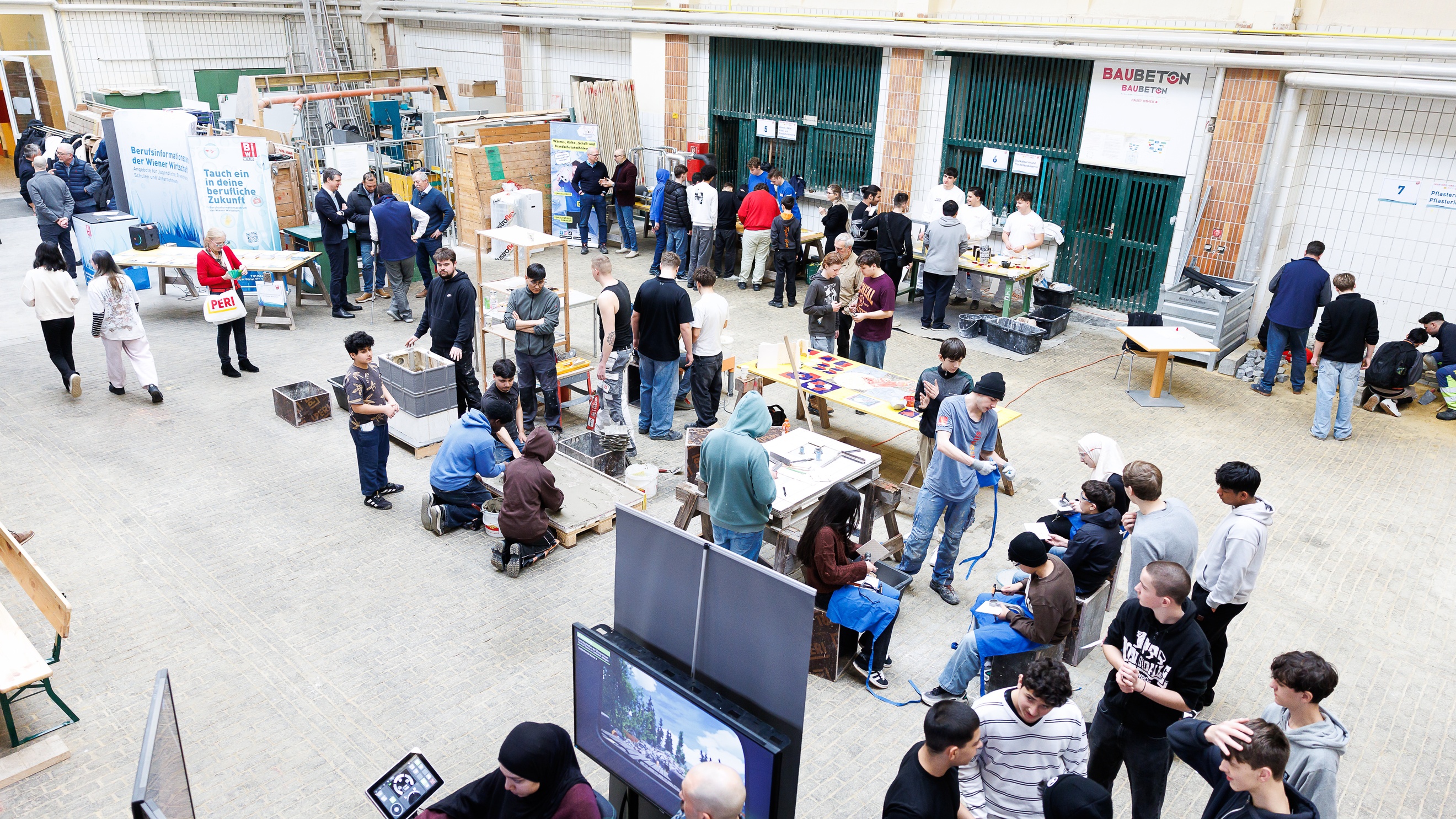 Aufnahme einer großen Halle, in der an verschiedenen Stationen erwachsene Personen und Jugendliche stehen. Auf einem Plakat steht Tauch ein in deine berufliche Zukunft und Berufsinformation