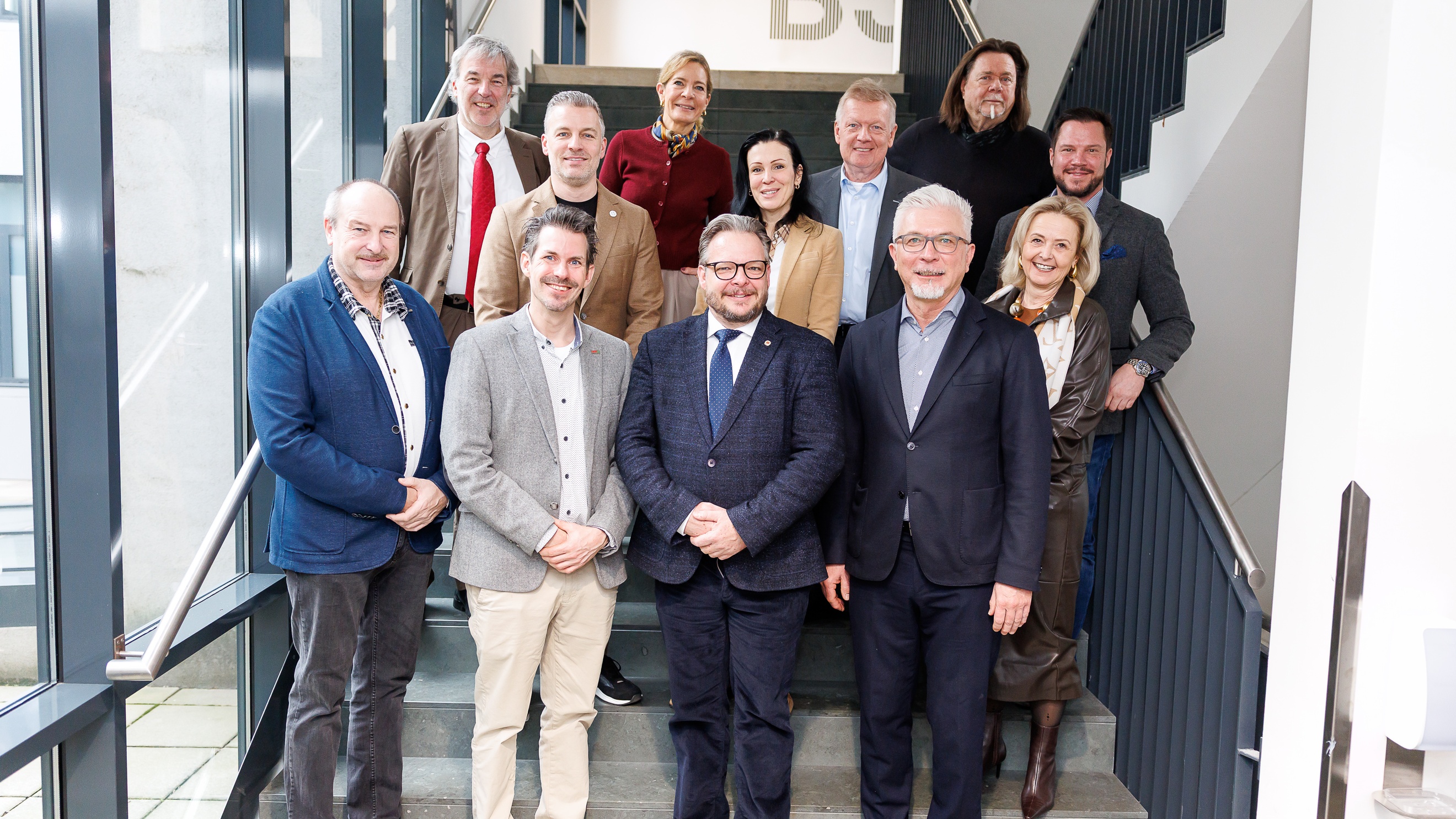 Porträt von mehreren Personen, die neben- und hintereinander auf Stiegen in einem Treppenhaus stehen