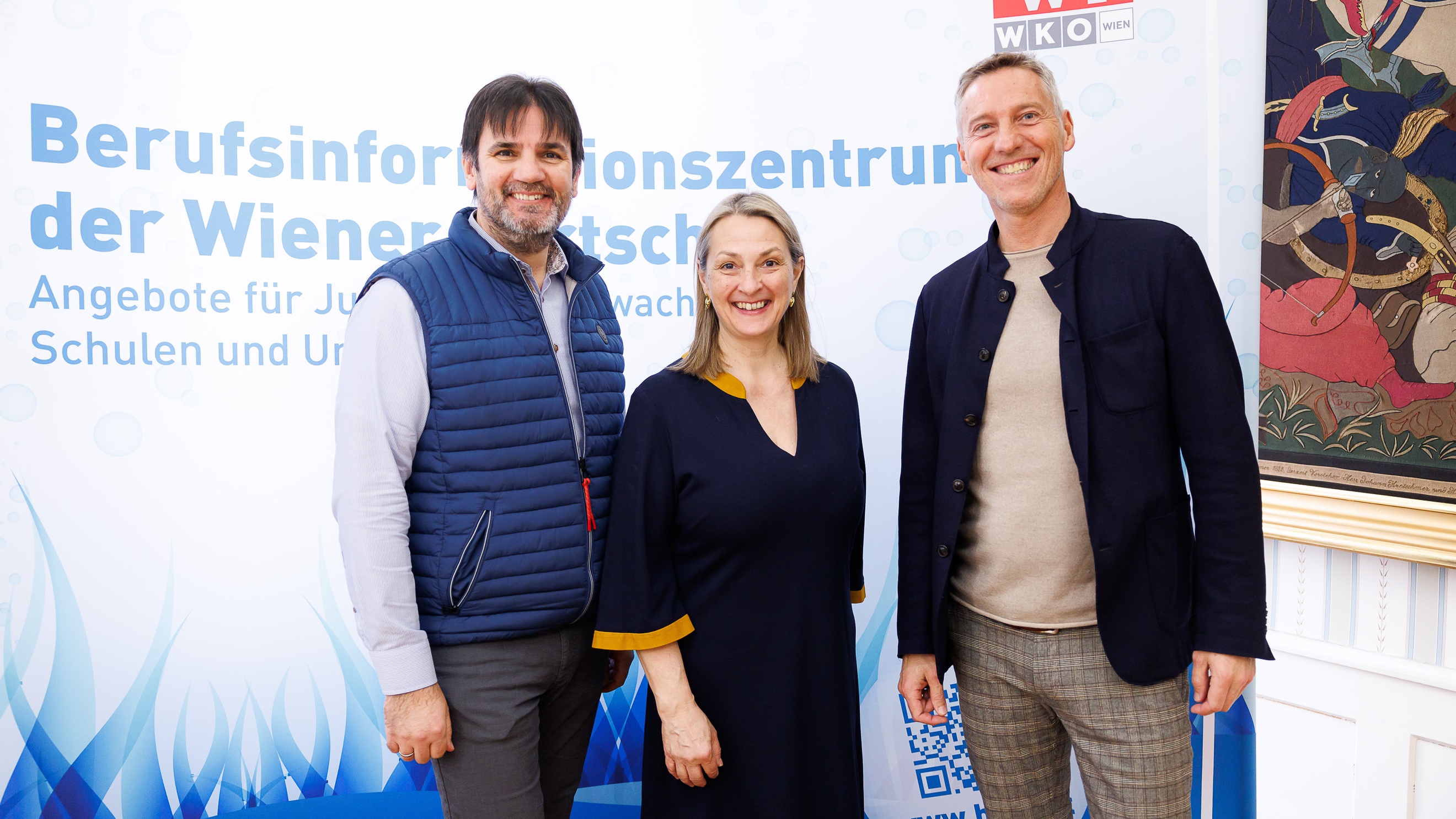 Porträt dreier nebeneinander stehender Personen. Hinter ihnen ist ein großer Banner, auf dem Berufsinformationszentrum der Wiener Wirtschaft steht