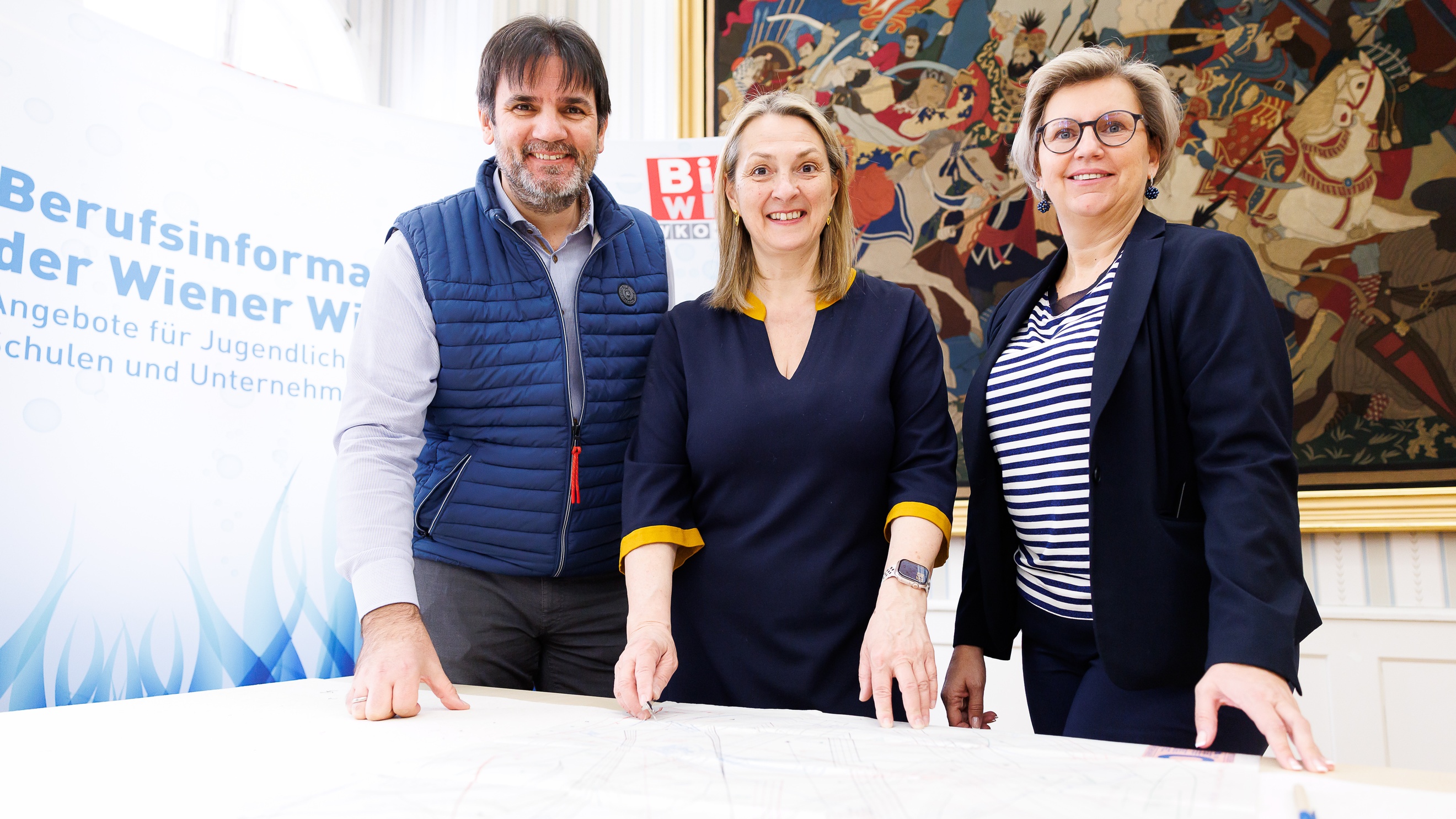 Porträt dreier nebeneinander stehender Personen. Hinter ihnen ist ein großer Banner, auf dem Berufsinformationszentrum der Wiener Wirtschaft steht