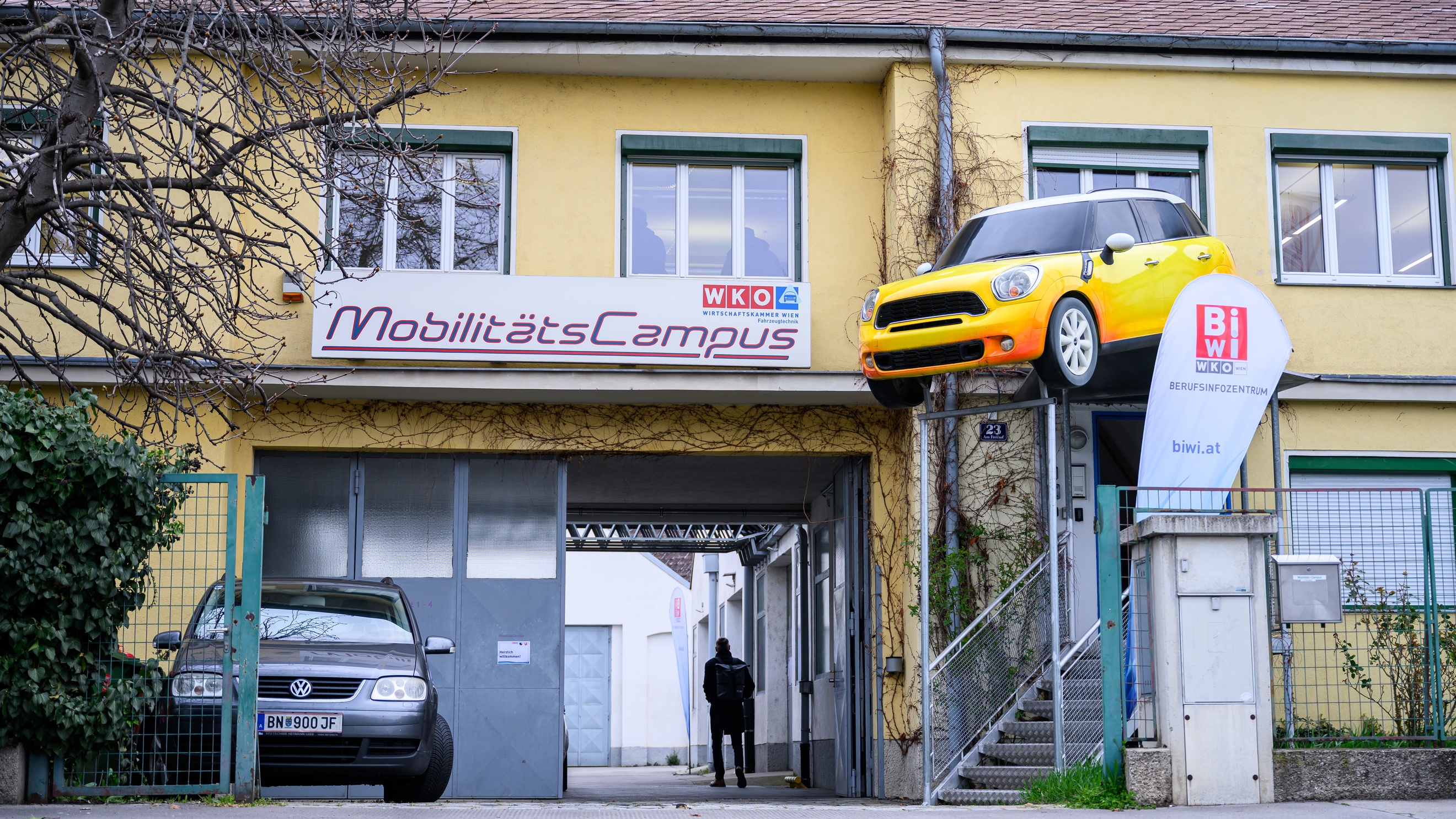 Fassade eines zweistöckigen Hauses mit einer Garageneinfahrt. Über der Einfahrt hängt ein Schild, auf dem Mobilitätscampus steht. Daneben ist ein Werbebanner, auf dem Biwi steht