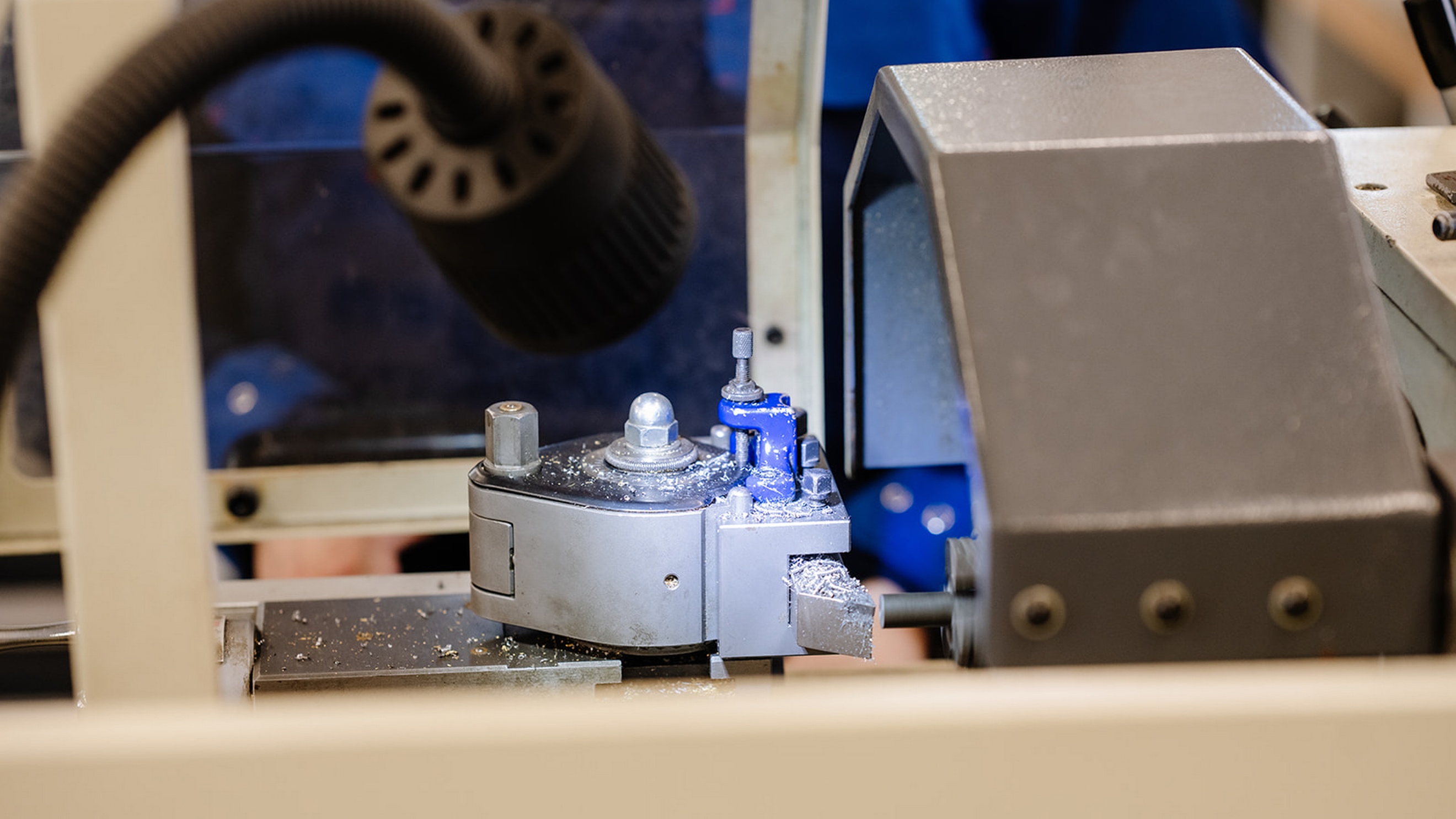 Nahaufnahme eines Werkzeugkopfs an einer technischen Maschine. Neben dem Werkzeug liegen Metallspäne auf der Arbeitsfläche. Ein schwarzer Lampenkopf beleuchtet den Arbeitsbereich