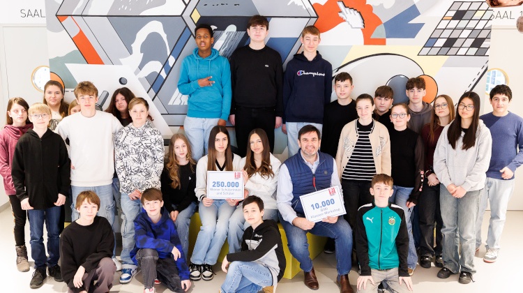 Gruppenfoto von vielen Teenagern, Kindern und einer erwachsenen Person vor einer bunten Wand. Manche Kinder und Teenager sitzen, andere stehen