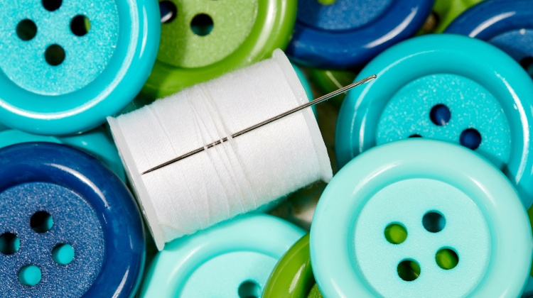 knöpfe in unterschiedlichen farben liegen nebeneinander, in der mitte befindet sich ein stecknadel und ein stoff