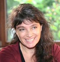 Frontale Aufnahme einer lächelnden Person mit dunklen Haaren sowie rotem Oberteil