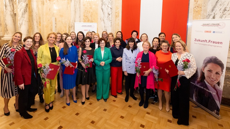 Eine Gruppe von weiblichen Personen steht in einem großen, hellen Raum mit Marmorsäulen vor einer rot-weiß-roten Österreich-Fahne. Rechts ein Roll-up mit der Aufschrift Zukunft.Frauen
